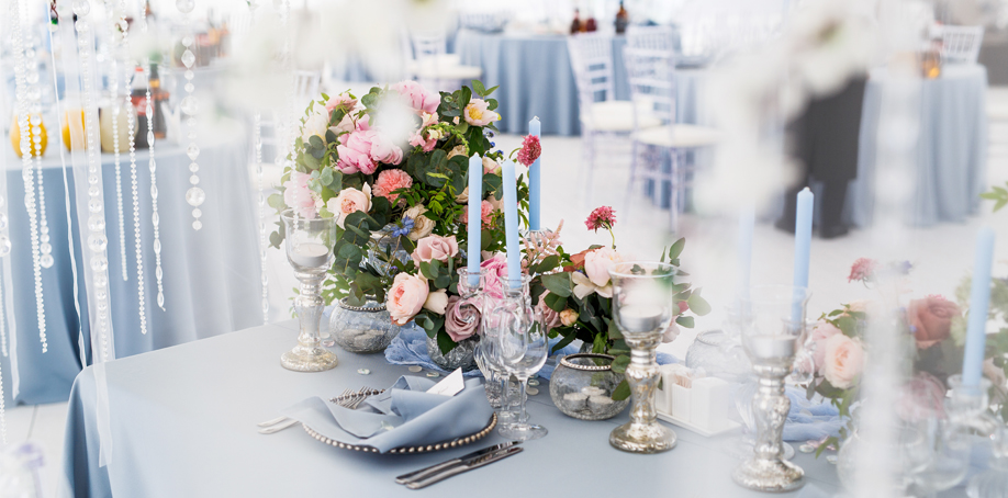 Dusty blue wedding reception table setting with napkin, charger plate, and flower arrangement