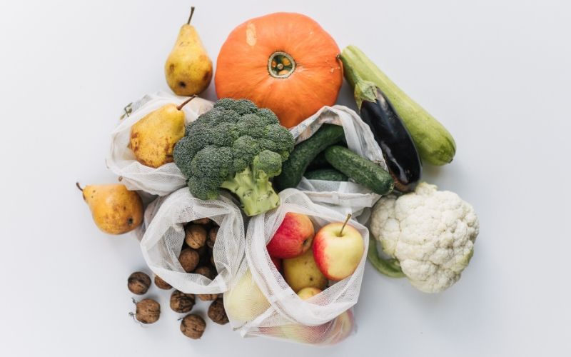 Auf einem weißen Tisch liegt frisches Obst und Gemüse, darunter Kürbis, Birnen, Äpfel und Walnüsse. Diese sind zum Teil in weiß transparenten Beuteln untergebracht.