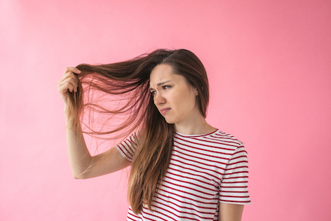 frau-vor-rosa-wand-mit-gestreiftem-shirt-haelt-haarstraehne-hoch-schaut-betruebt
