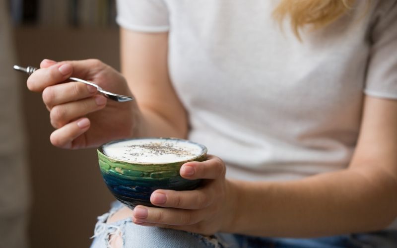 Frau hält kleine Schale mit Joghurt in der Hand. In der anderen hat sie einen Löffel.