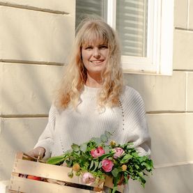 blonde-frau-haelt-obstkiste-mit-blumen-und-einkaeufen-in-derhand-lacht