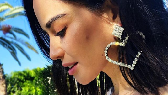 Edy Ganem wearing jewel-encrusted oversize heart shaped May Earrings by J.ING women's fashion