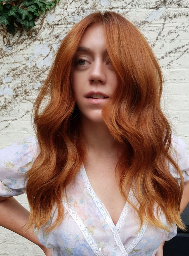 A woman with long red hair posing in front of a brick wall - Josh Wood Hair Colour Expert