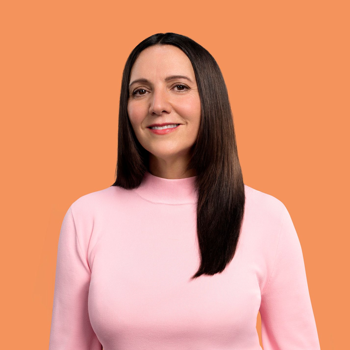 A woman wearing a pink sweater and orange background - Josh Wood Hair Colour Expert