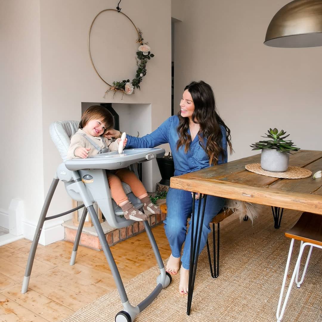 A woman sits at a table with a baby in a high chair - Josh Wood Hair Colour Expert