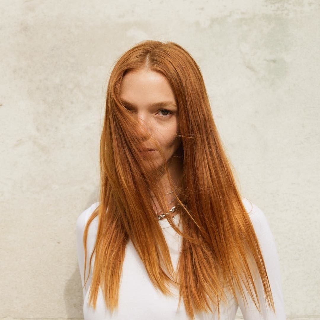 A woman with red hair posing against a wall - Josh Wood Hair Colour Expert