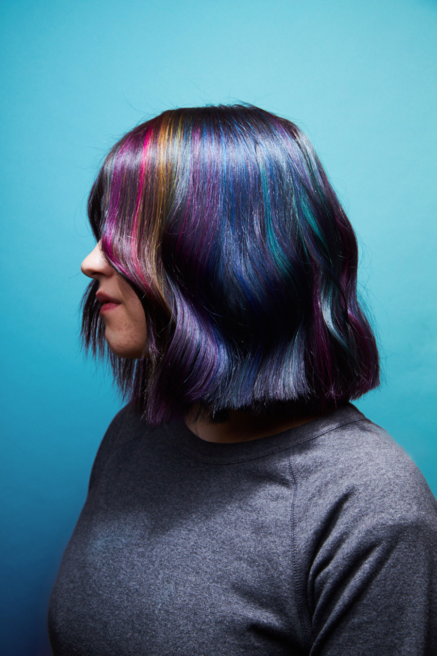 A woman with a rainbow coloured hair in front of a blue background - Josh Wood Hair Colour Expert