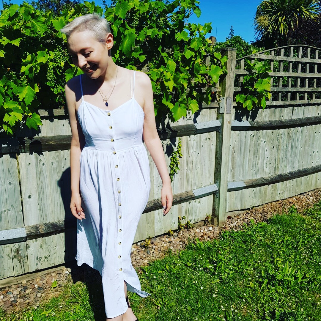 A woman in a white dress standing in front of a fence - Josh Wood Hair Colour Expert