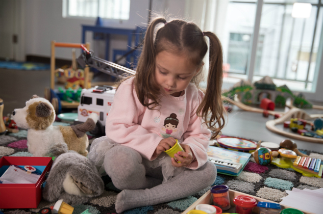 Little girls sits in a playroom surrounded by toys