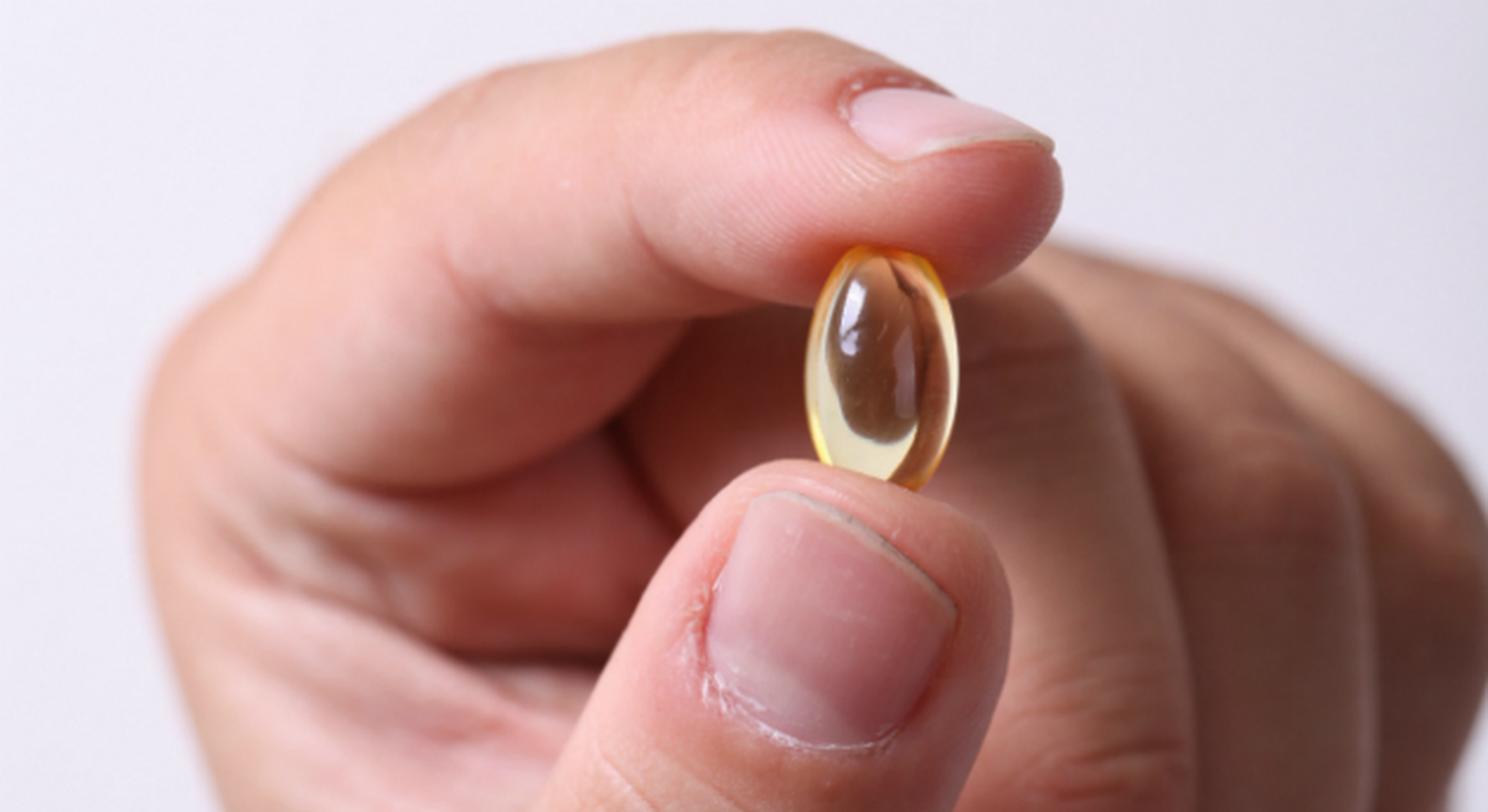 Hand holding a yellow capsule vitamin pill