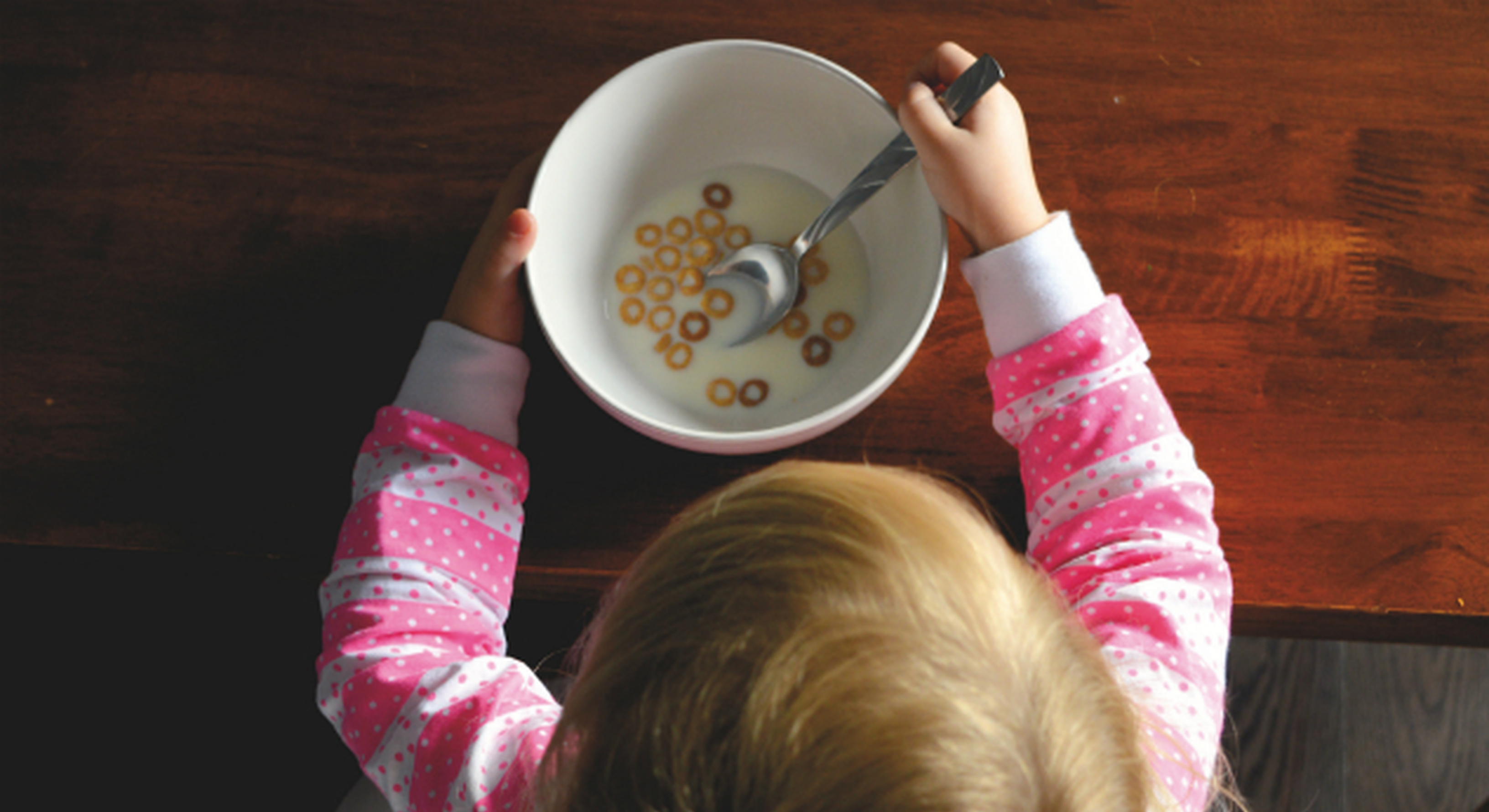 Little girl eating bowl of Cheerios and milk