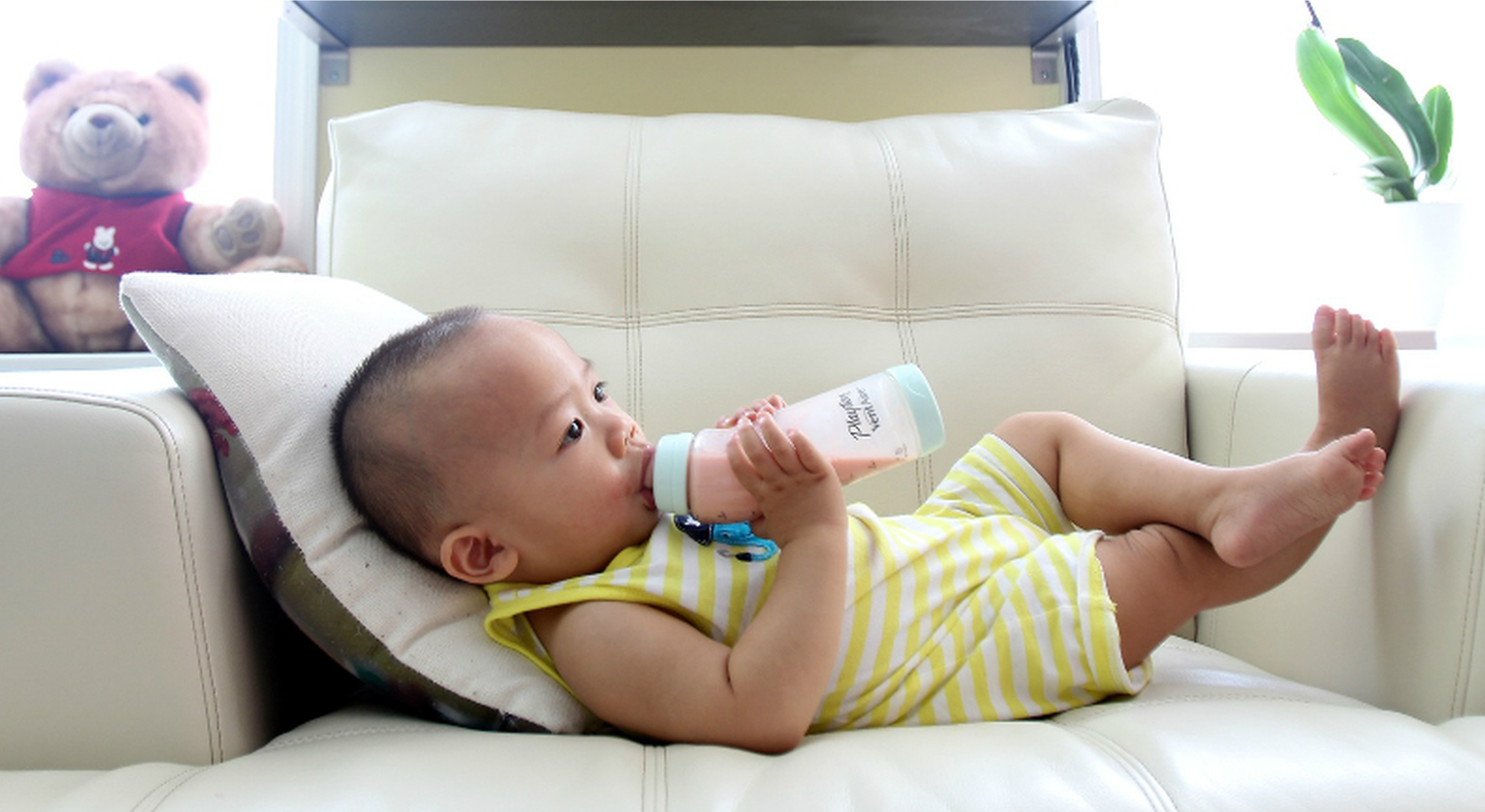 Toddler on sofa drinking pink liquid from a nursing bottle