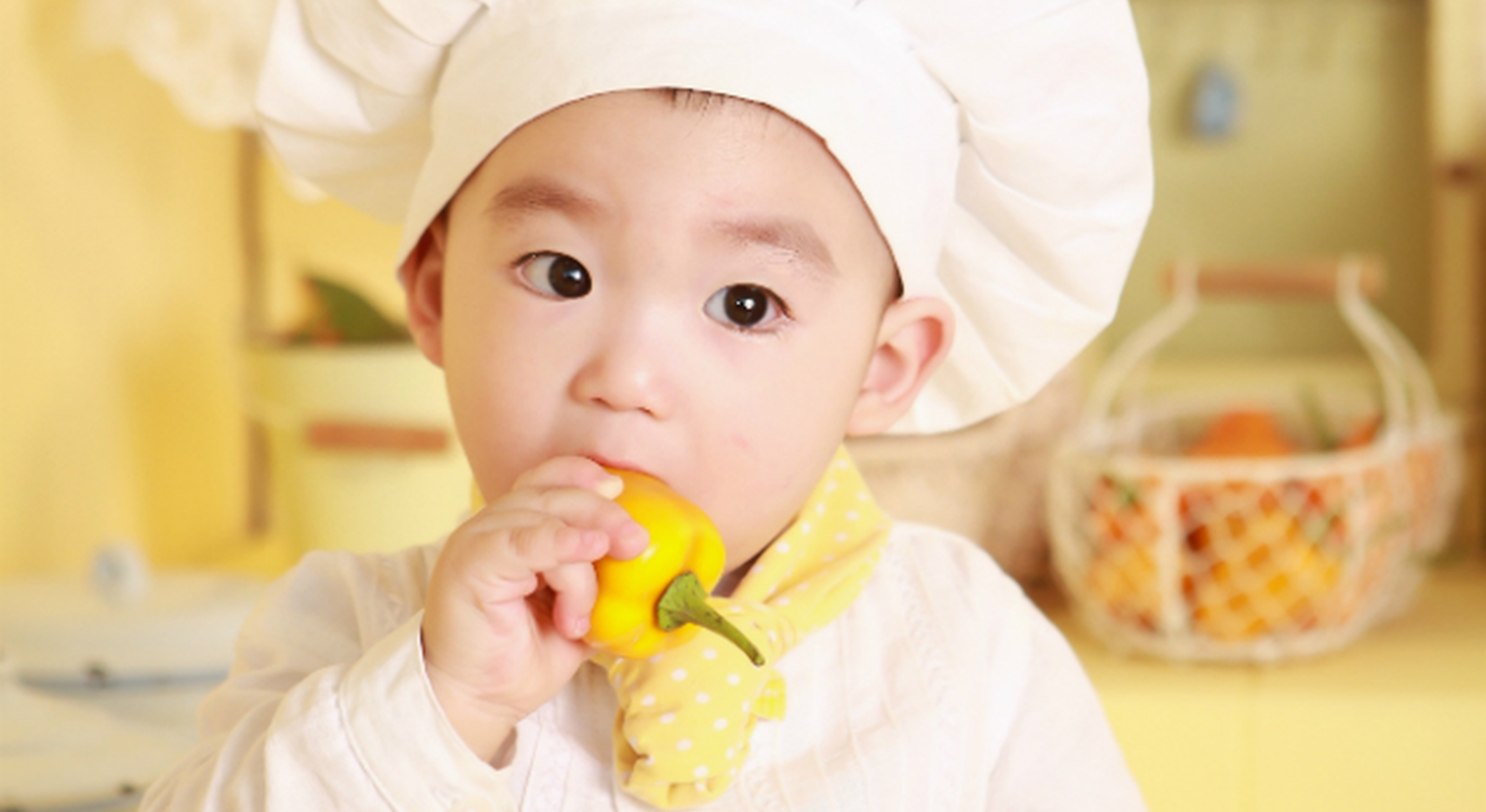 Little boy in chef hat eating yellow pepper