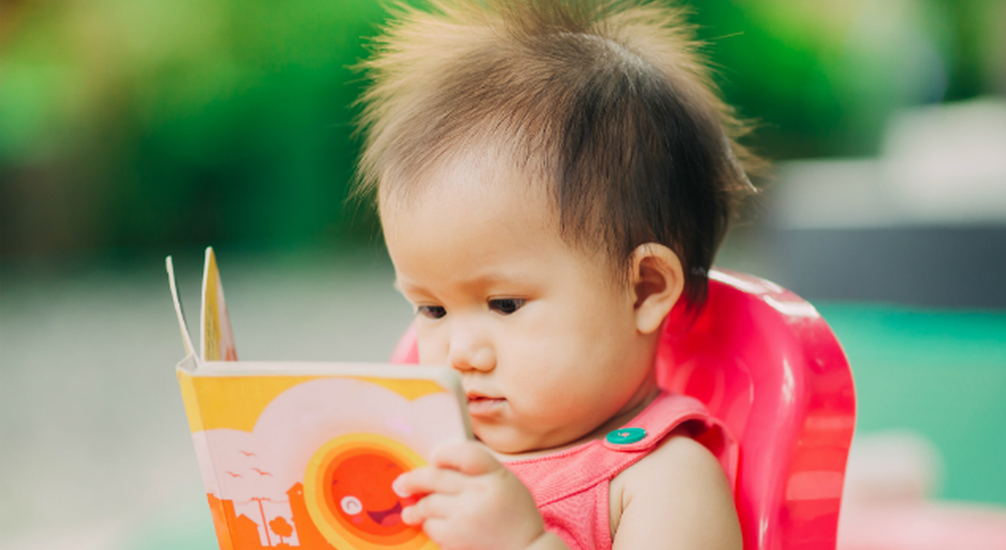 Toddler reading a book outside