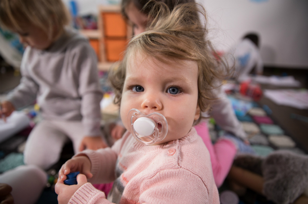 Toddler sits and sucks a pacifier